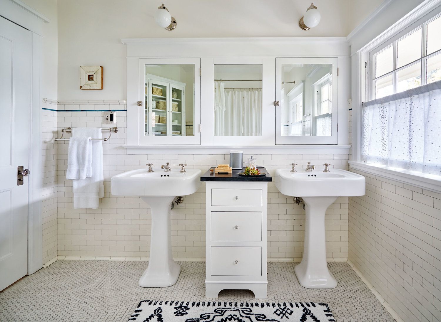 The main bath has twin pedestal sinks and medicine cabinets as well as original white tile on the walls and floor.