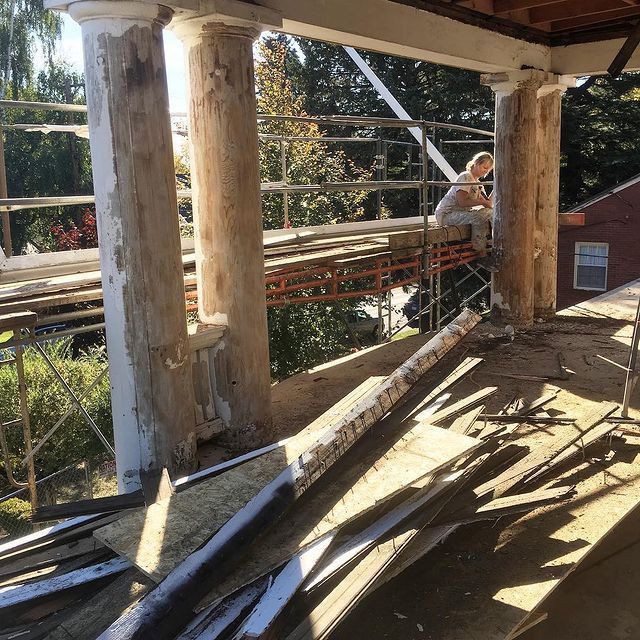 A woman is sitting on a scaffolding on the porch of a building under construction.