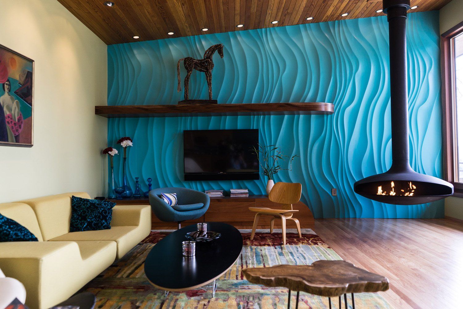 A vivid turquoise wall has a wave-like texture, setting off custom walnut built-in shelves & a fir ceiling in the living room.