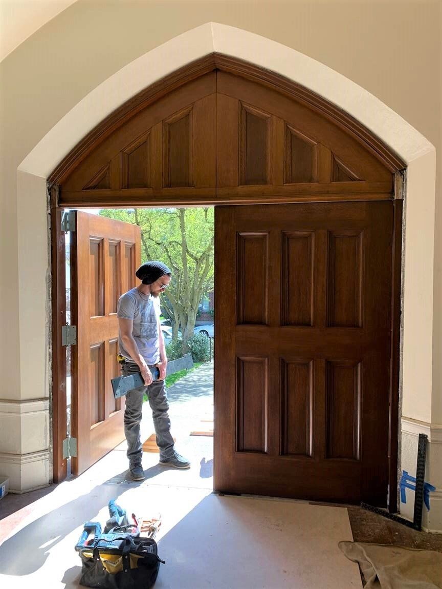A man is standing in front of an open wooden door.