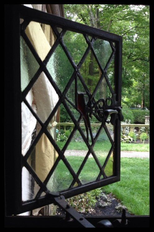 Open black diamond-patterned window in front of a green garden and stone path