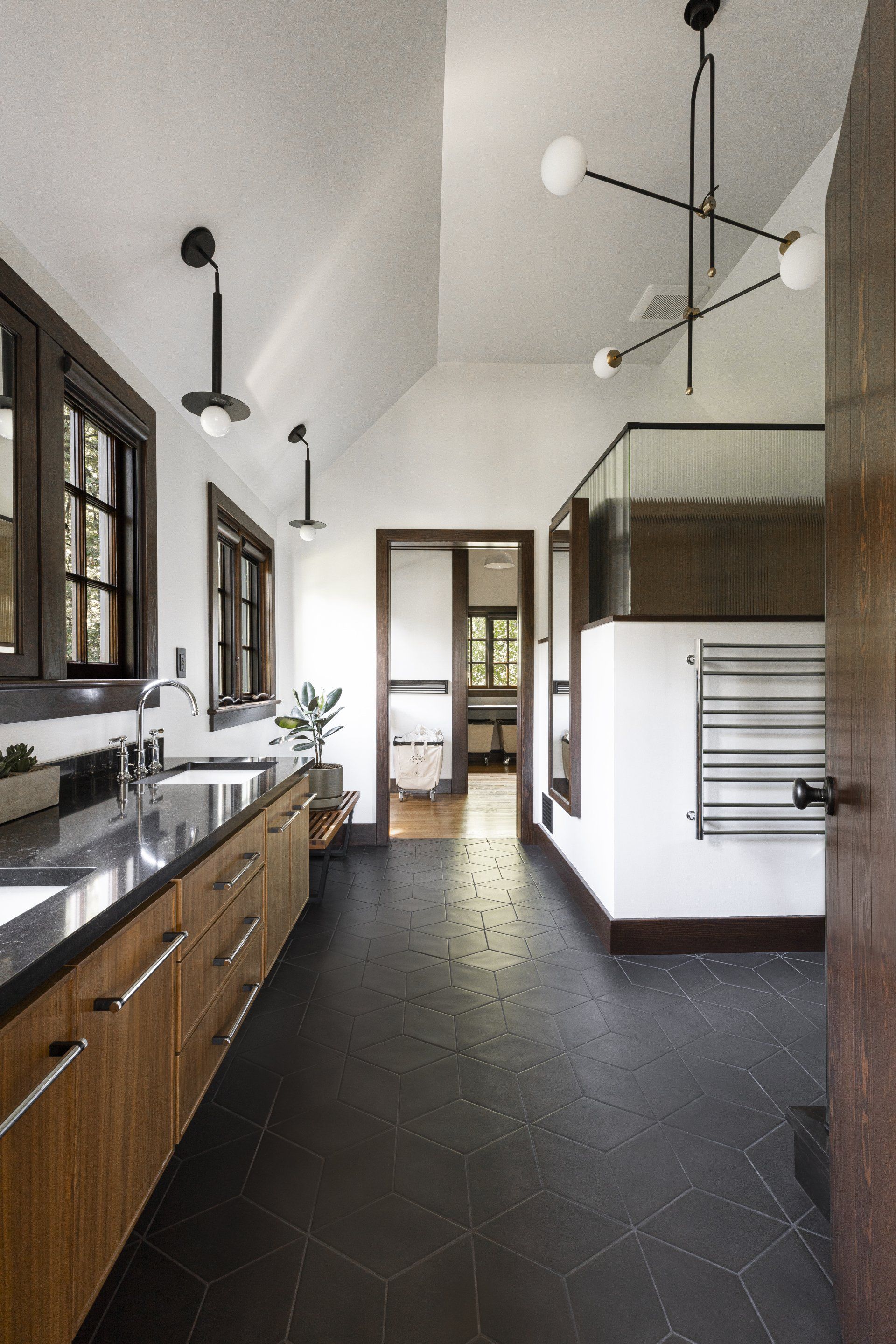 Looking from the bedroom in to the main bathroom with its soaring ceiling, black matte floor tile and walnut cabinetry. 
