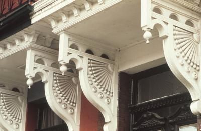 Ornate white wooden brackets and trim under a building eave with dark windows and red wall panels