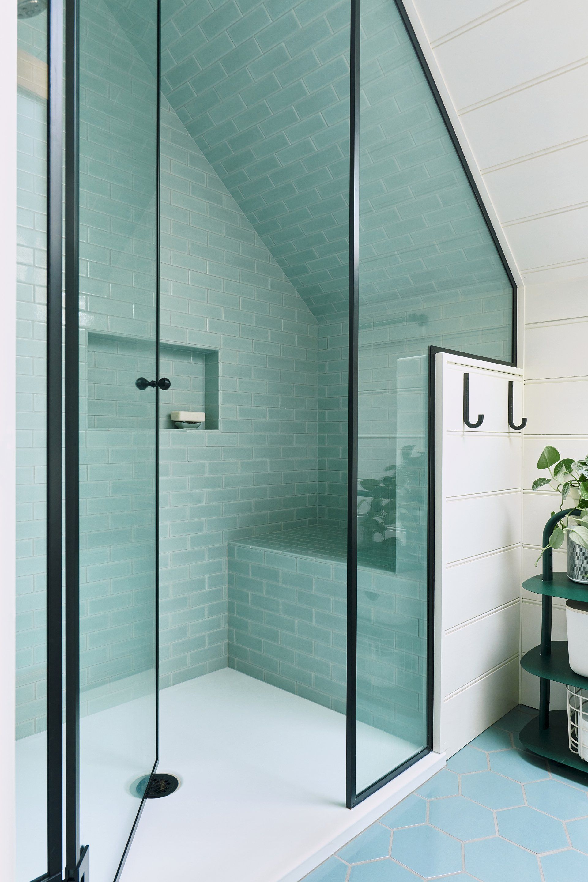 Opposite the sink and door, a roomy shower tiled in ocean hues has a smart under-eave shower bench in the 2nd floor bath.