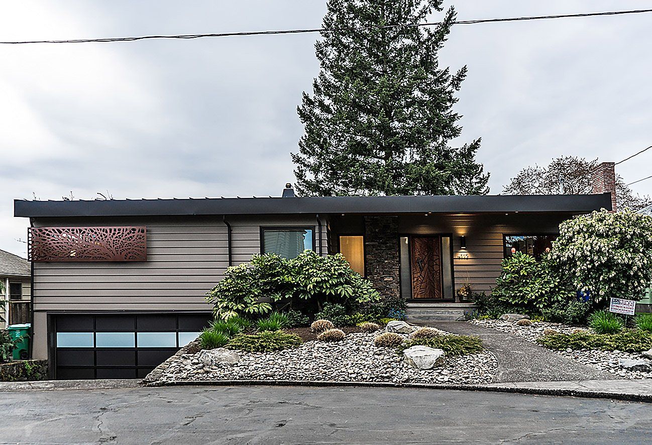 A house with a black garage door is sitting on top of a hill.