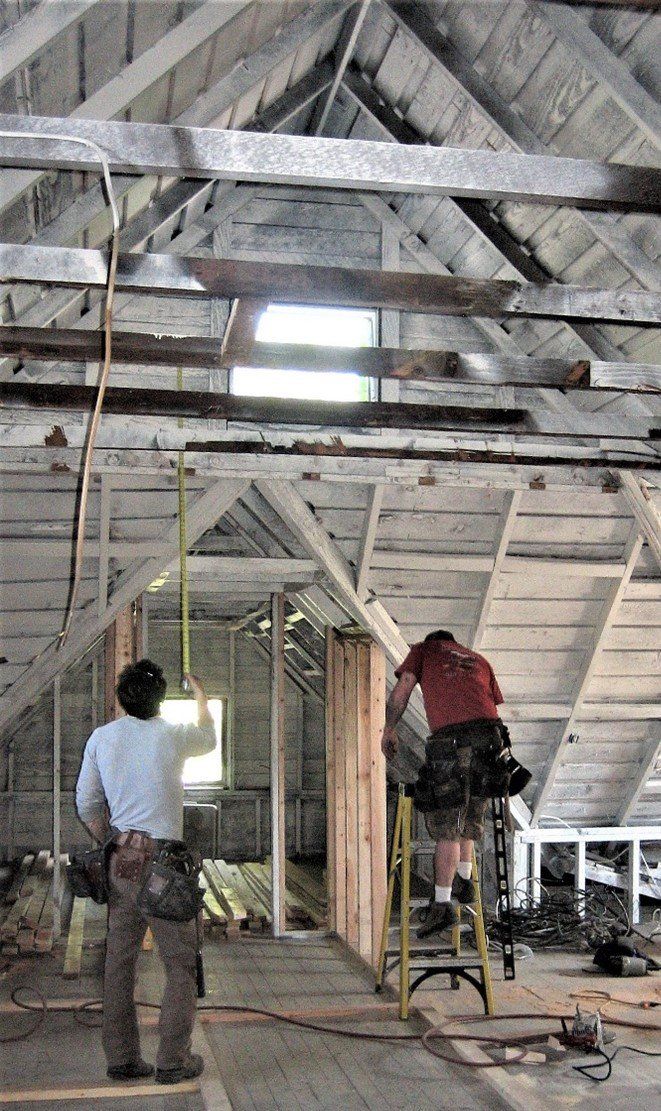 A man is standing on a ladder in an attic.