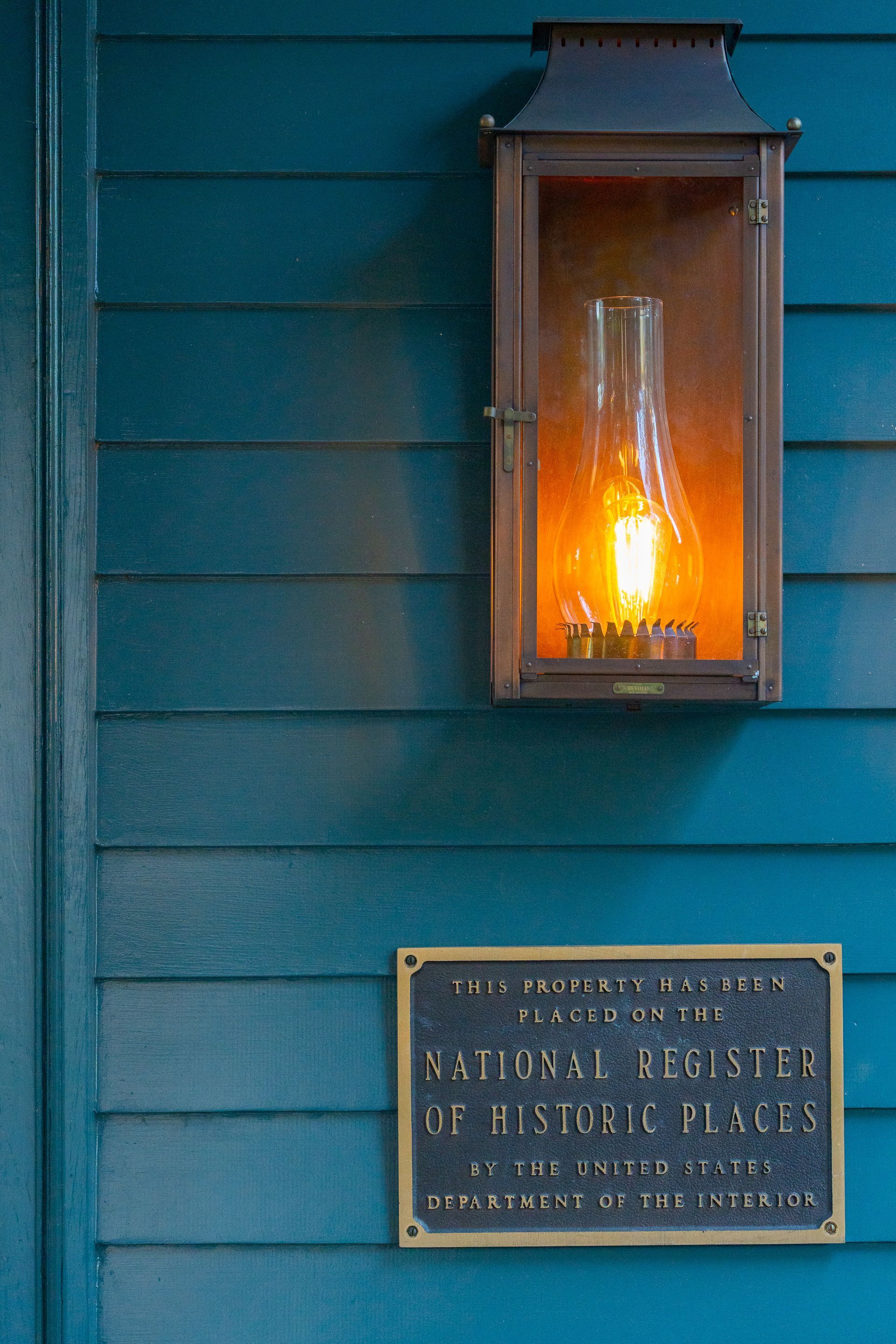 National Register of Historic Places plaque below copper lantern style sconce mounted to dark teal lap siding.