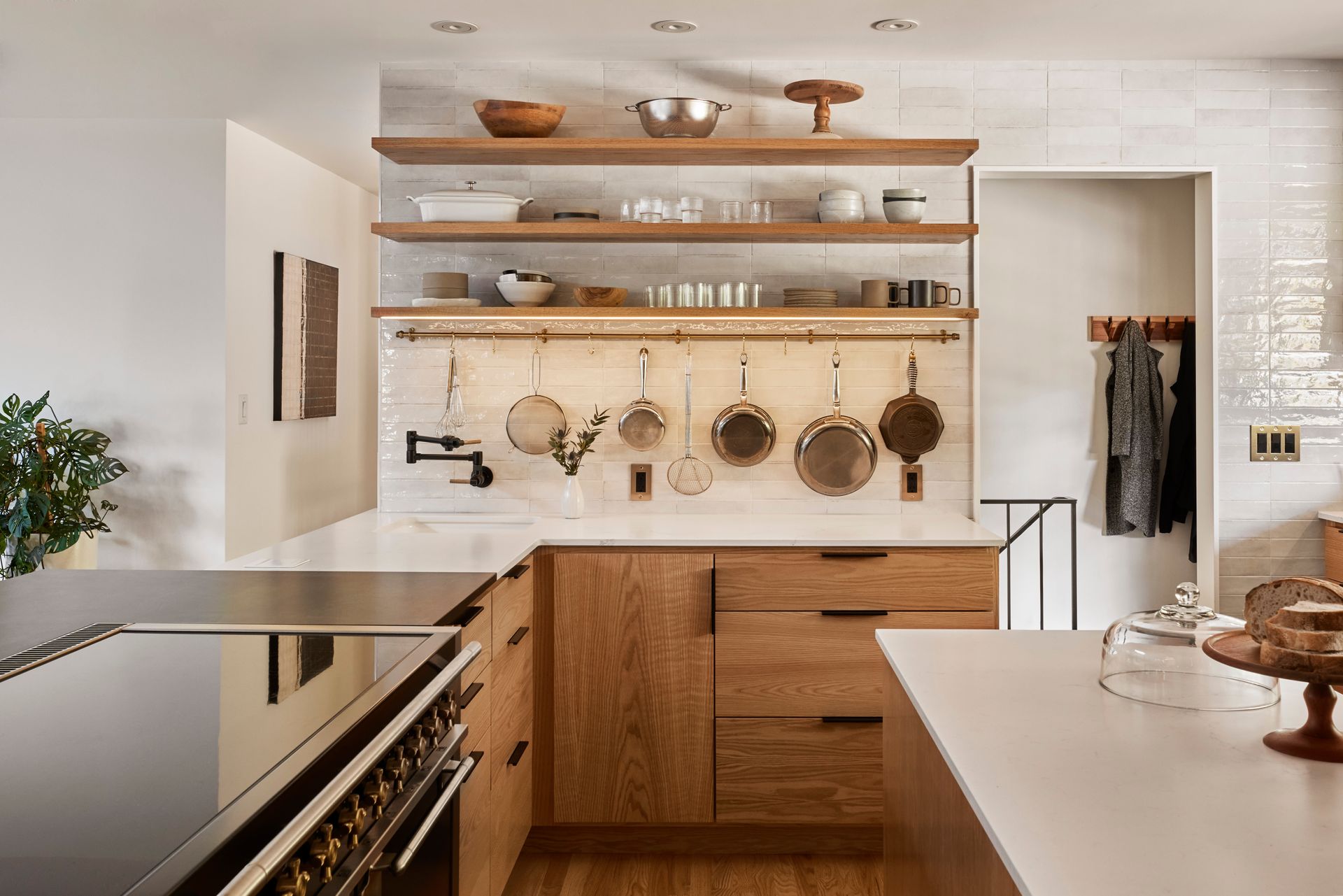 Close up of a bank of lower wood cabinets with open shelving above and a brass rail at the backsplash for favorite pots and utensils.