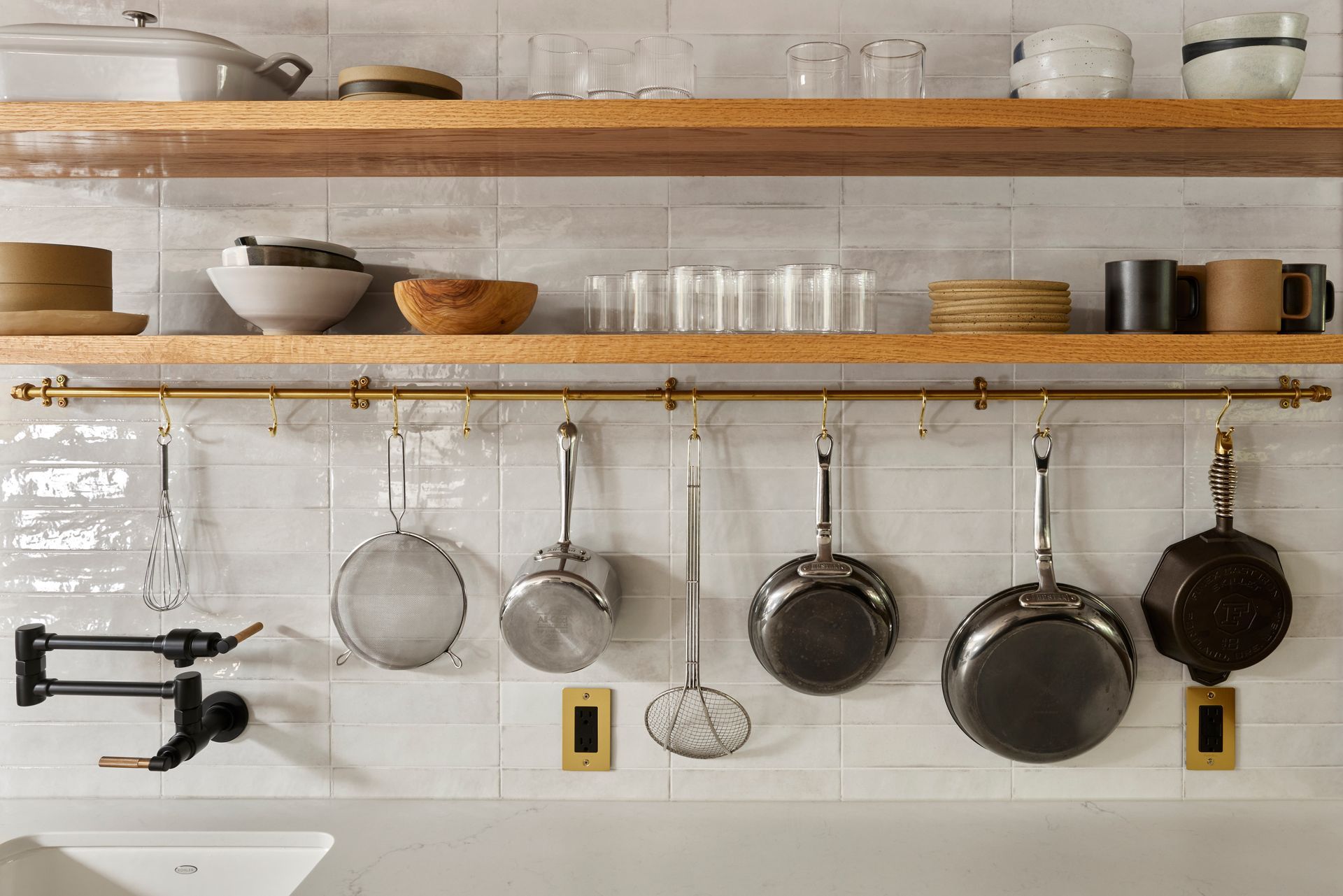Detail of the shelving and brass pot rail on a glossy white tiled wall in the midcentury kitchen. 