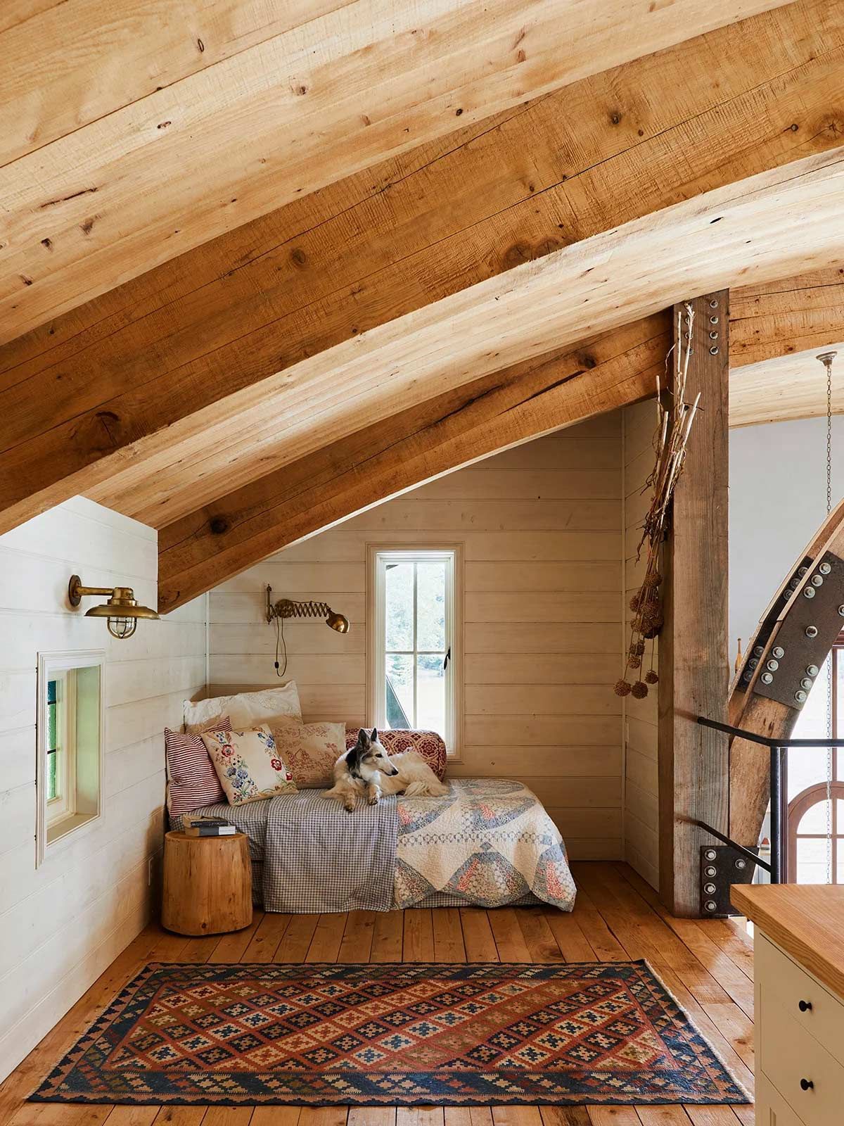 A dog is sitting on a bed in a room with wooden beams.