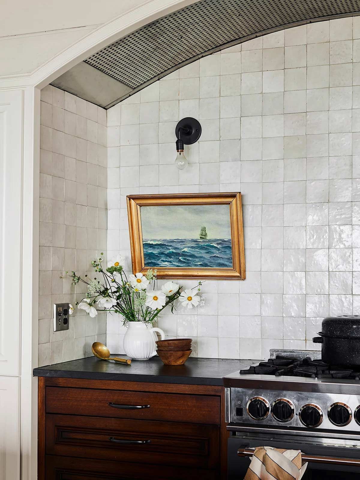 A kitchen with a painting on the wall above the stove.