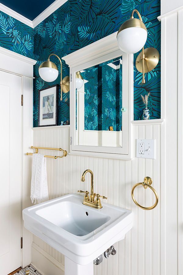 The main floor bathroom has a pedestal sink, mirror and palette of deep sea blues and greens with popping white trim and wainscoting.
