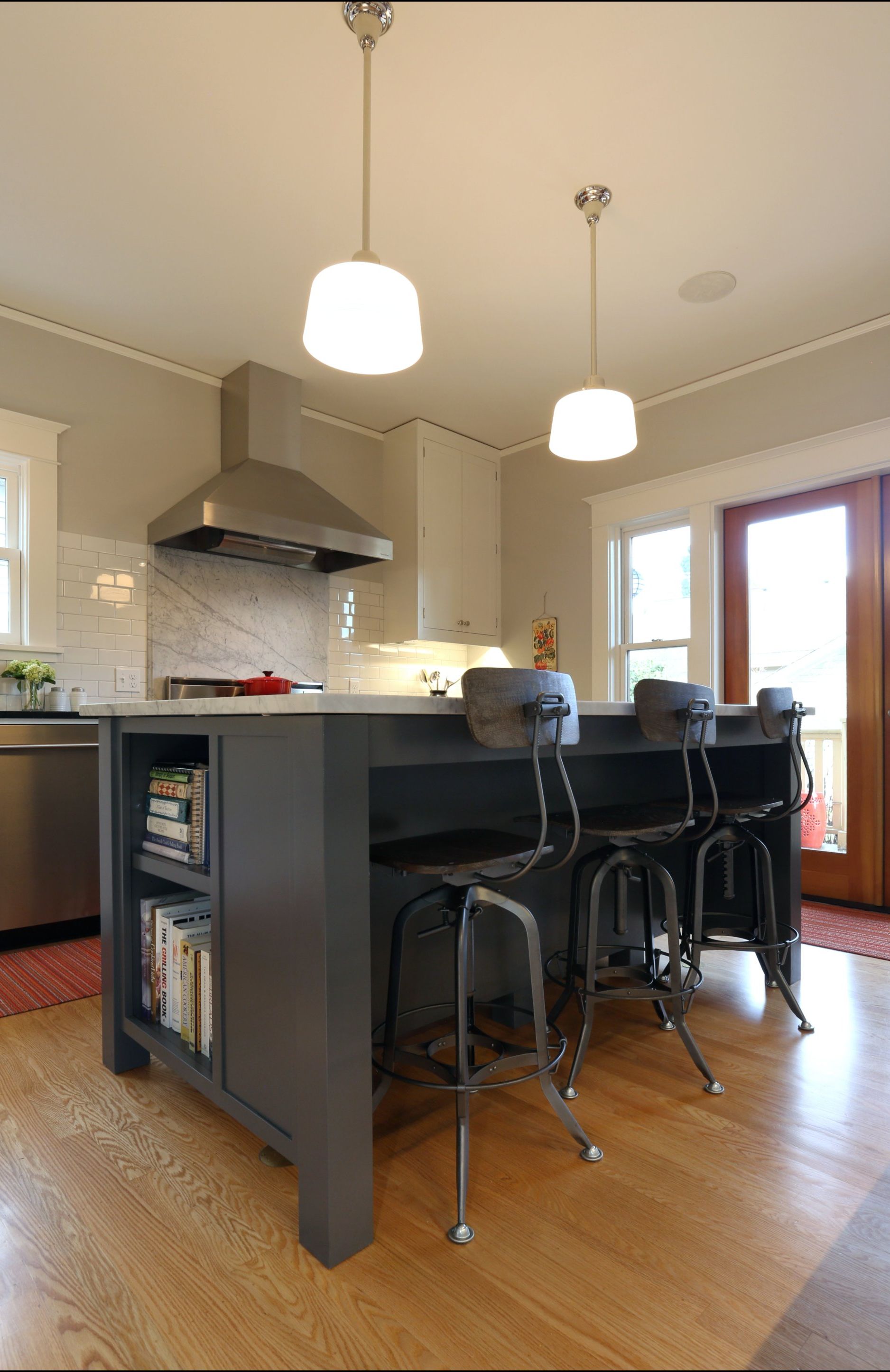 Kitchen with island, black stools, pendant lights, and hardwood floor, viewed from a dining area