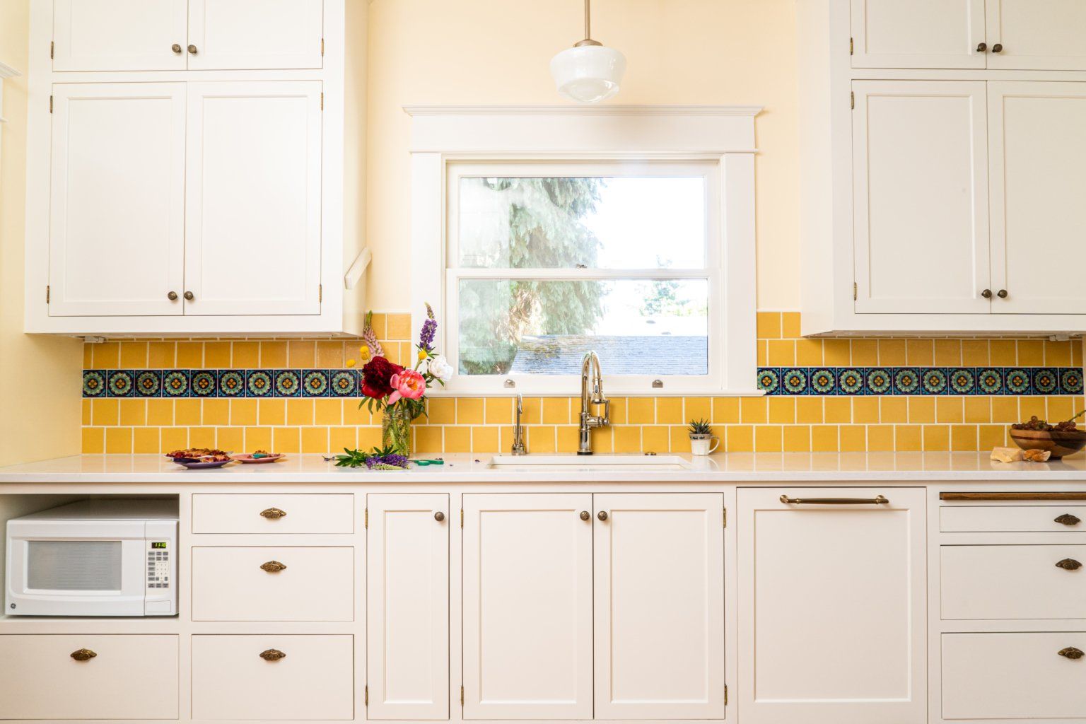 A kitchen with white cabinets and yellow tiles.