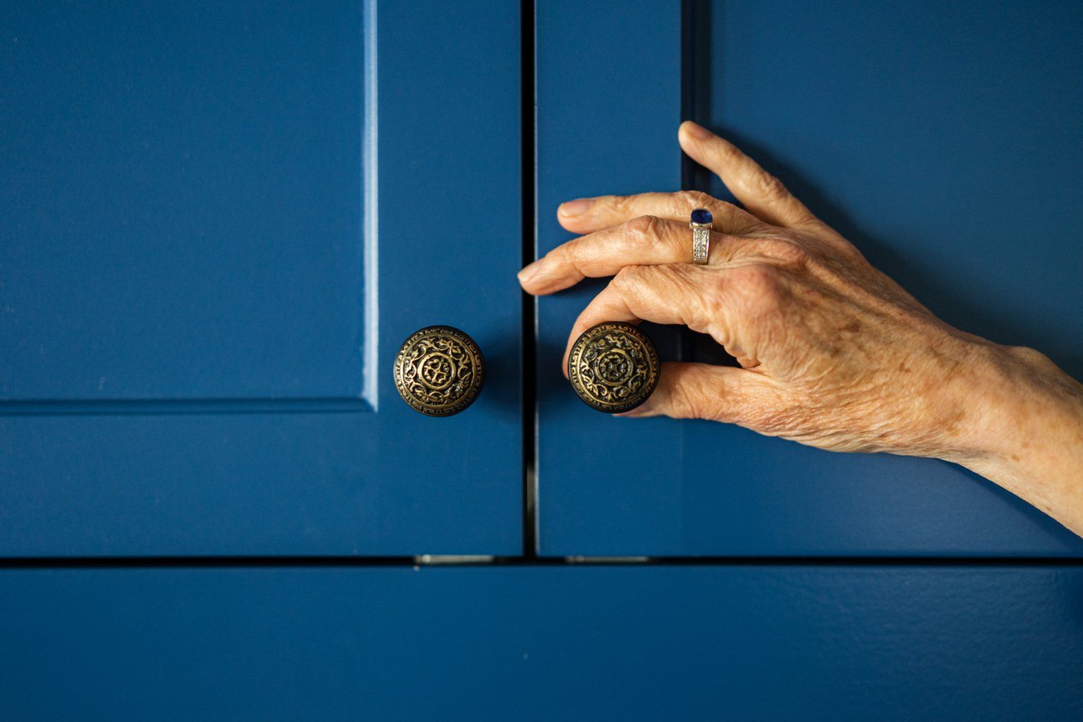 A woman with a ring on her finger is opening a blue cabinet door.