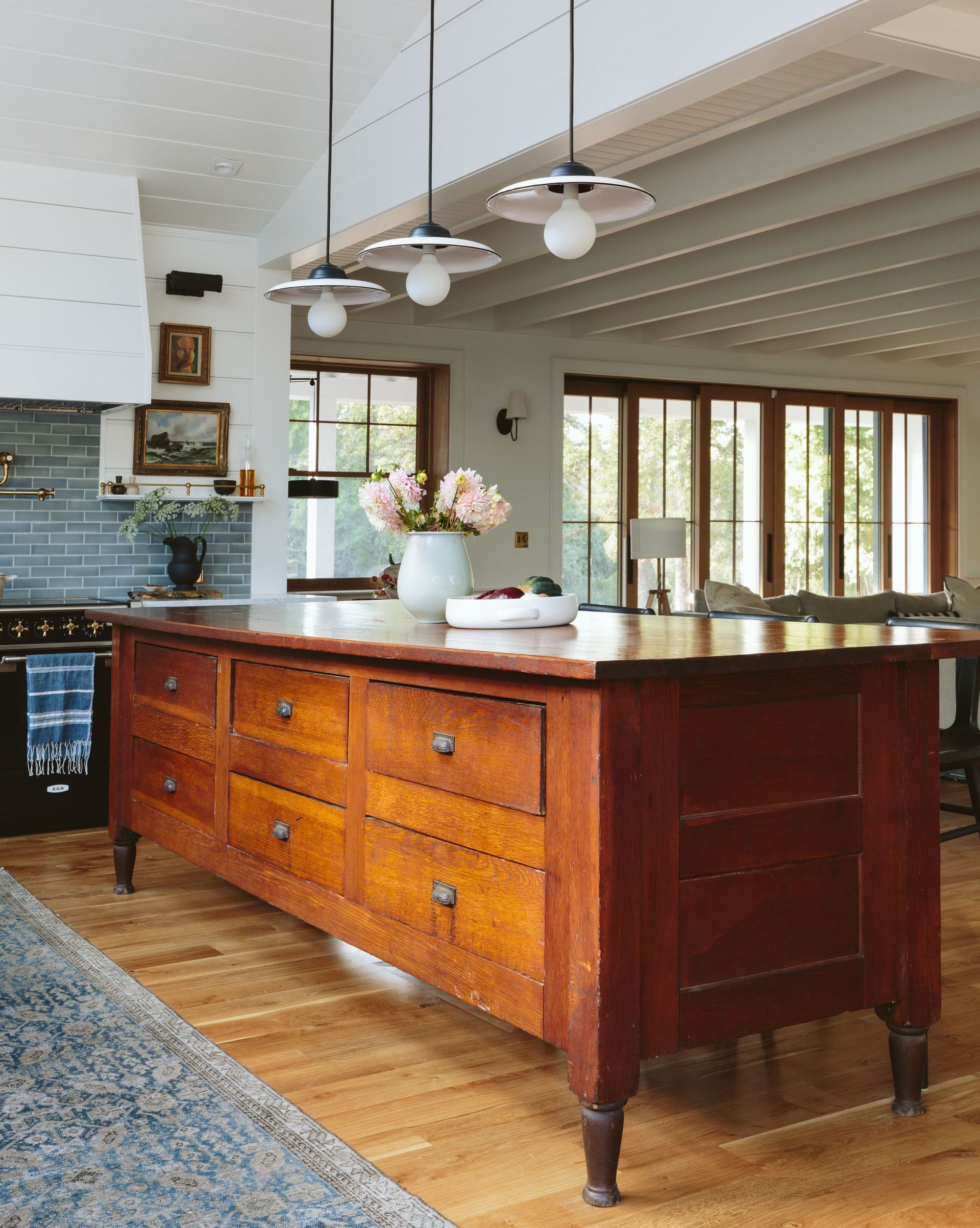 Kitchen with a large, dark wooden island, light wood floors, and white ceiling with pendant lights.