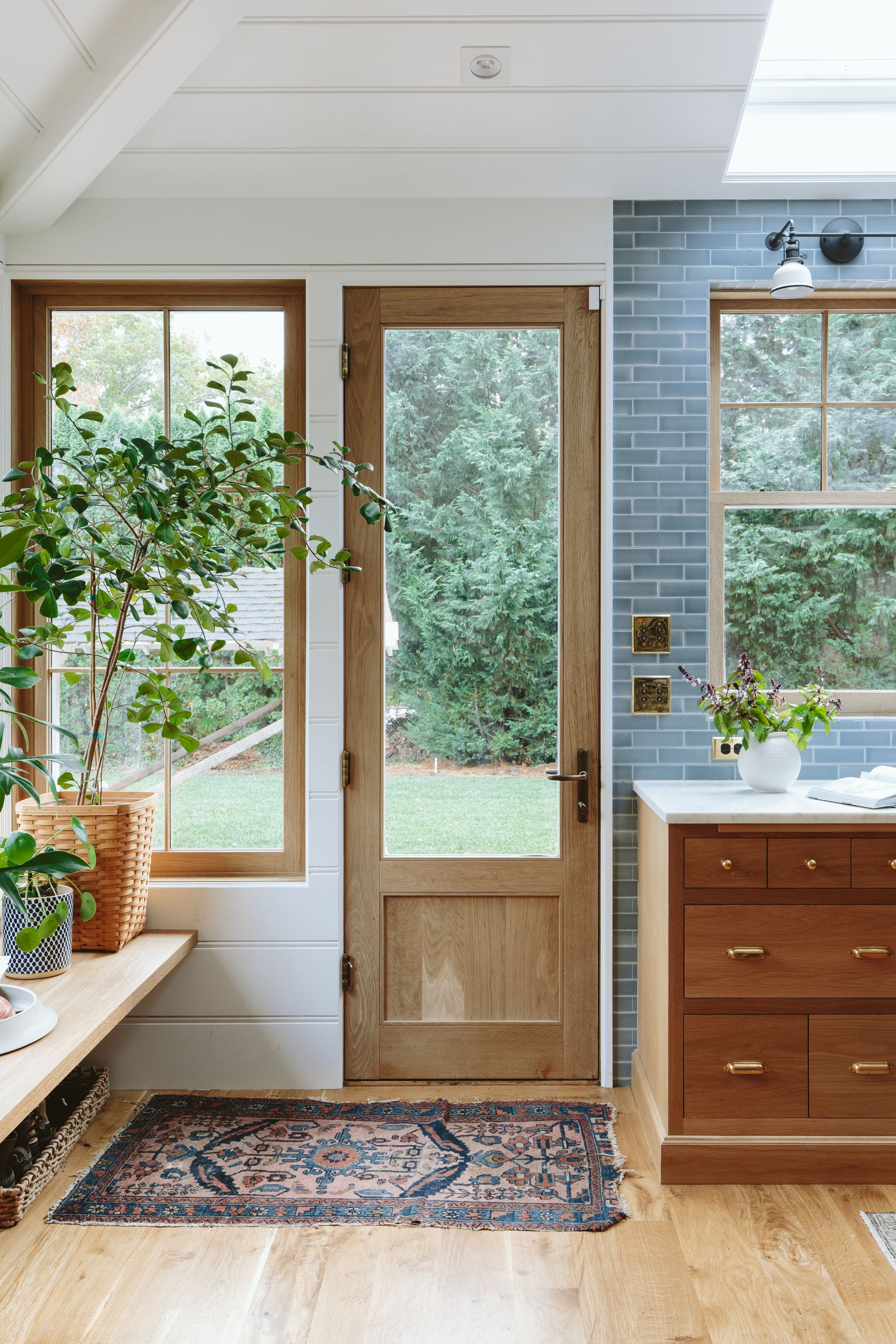 A back entrance featuring a change in wall finish from tile to v-groove paneling. A tall Oak door flanked by a large window and deep Oak bench.