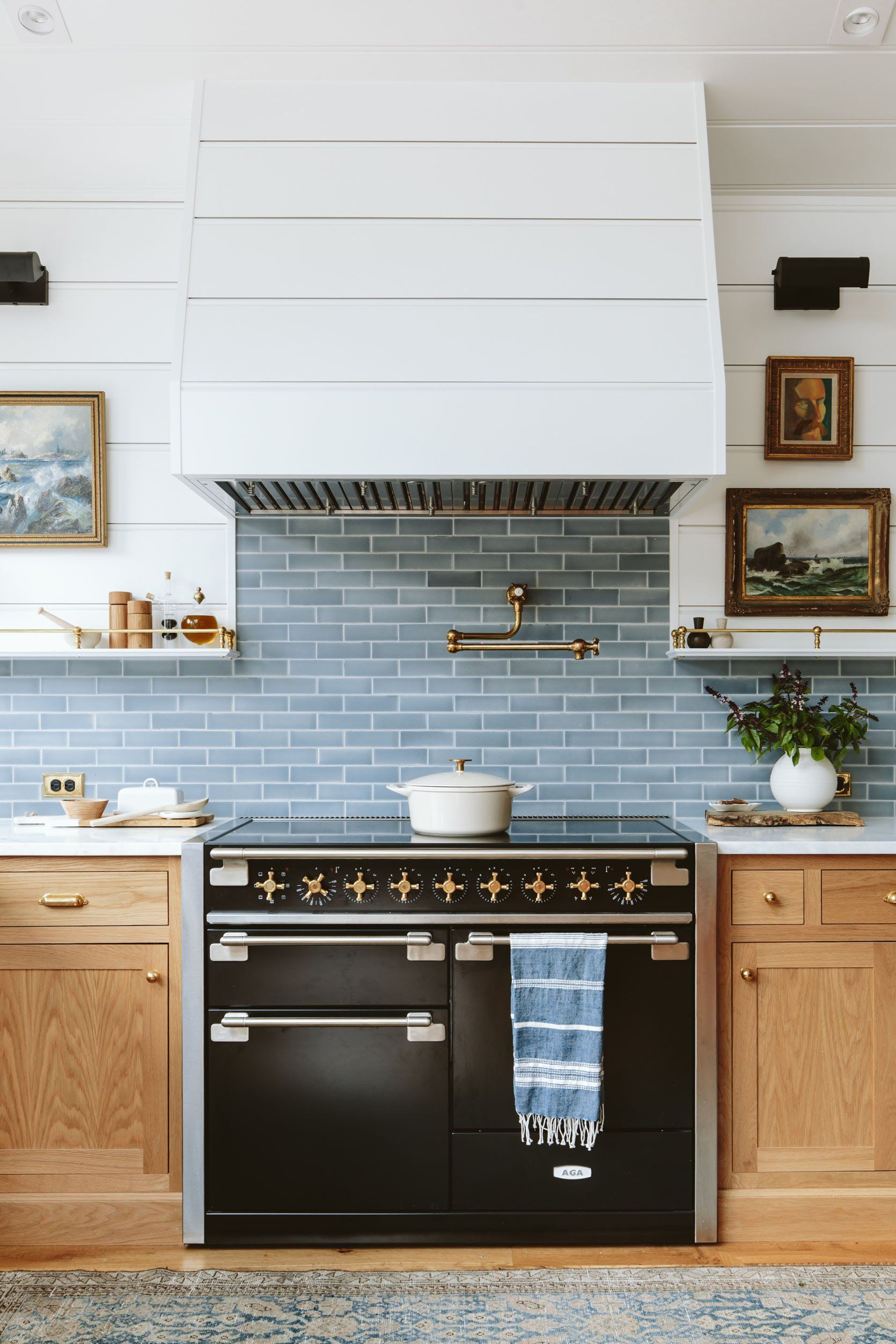 Black oven in a kitchen with blue tile backsplash, white hood, and wooden cabinets.