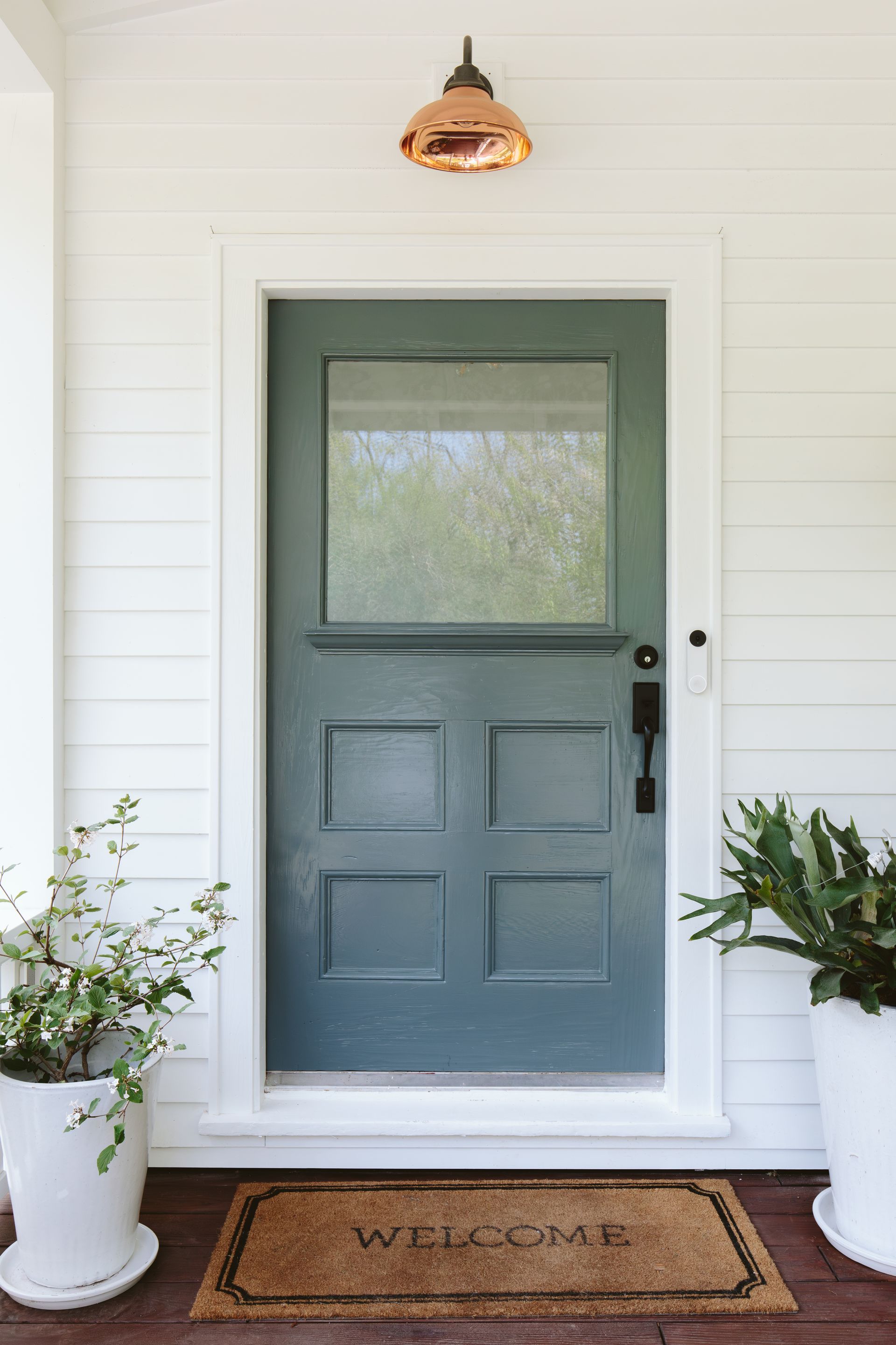 Vintage blue-green front door with welcome mat and copper shaded sconce.