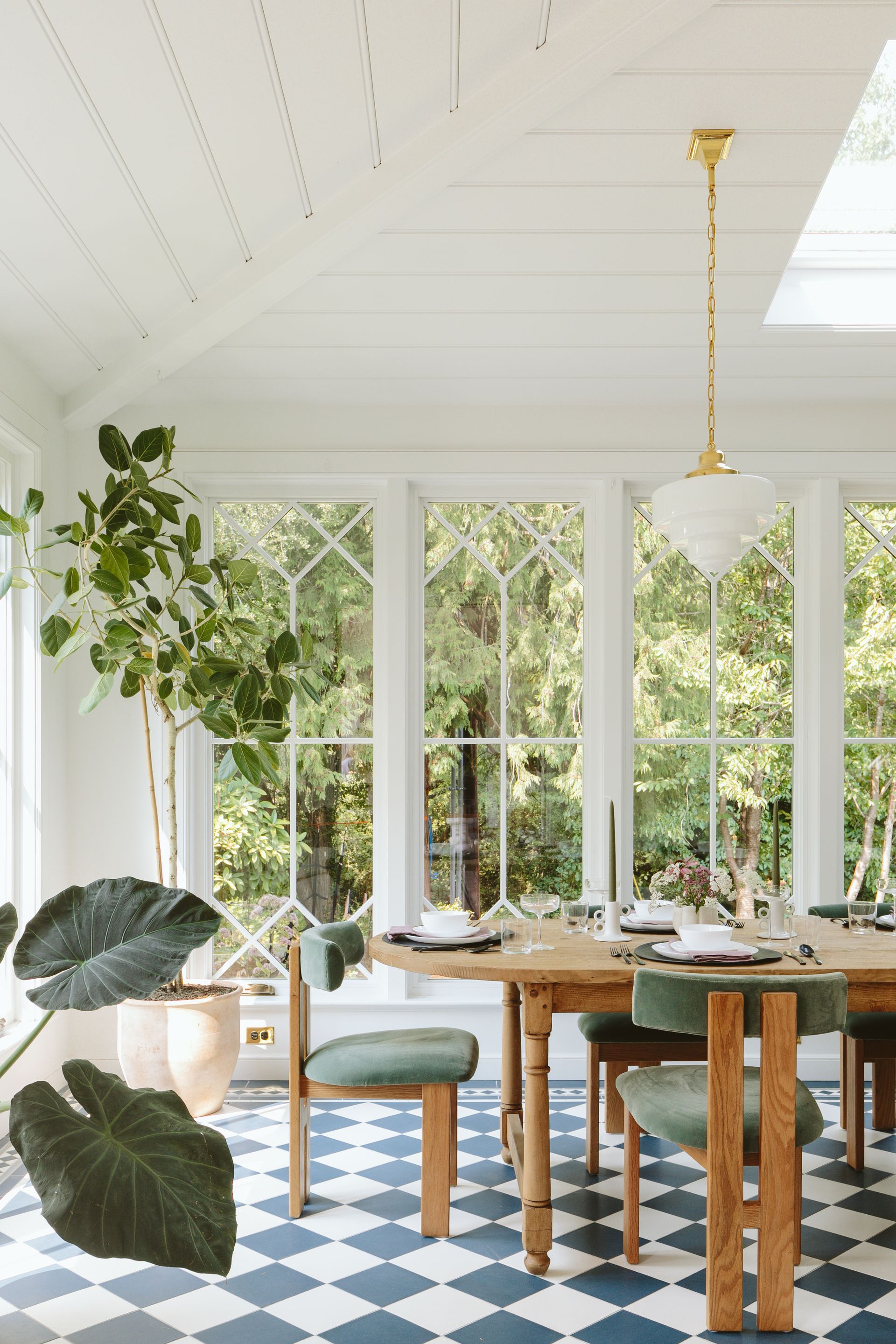 Sunroom with blue and white checkered tile floor with border, large windows with diamond shaped lites, contemporary dining chairs and a vintage table.
