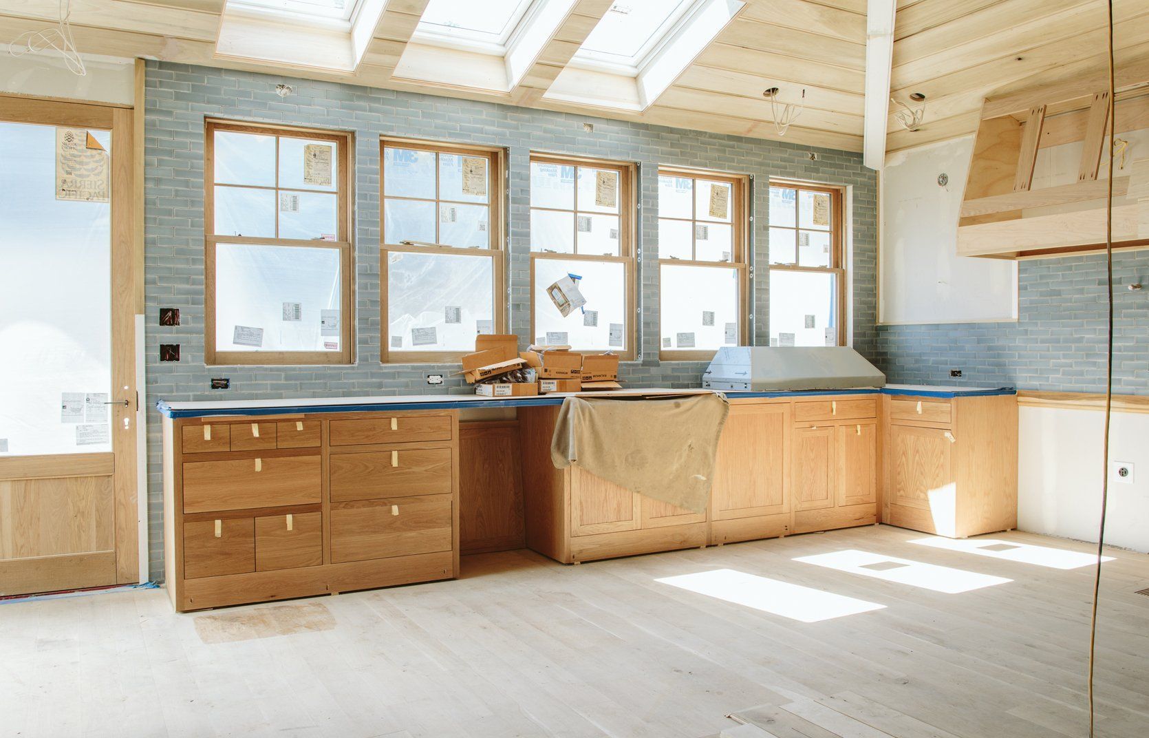 Light-filled kitchen under construction with wood cabinets and three windows.