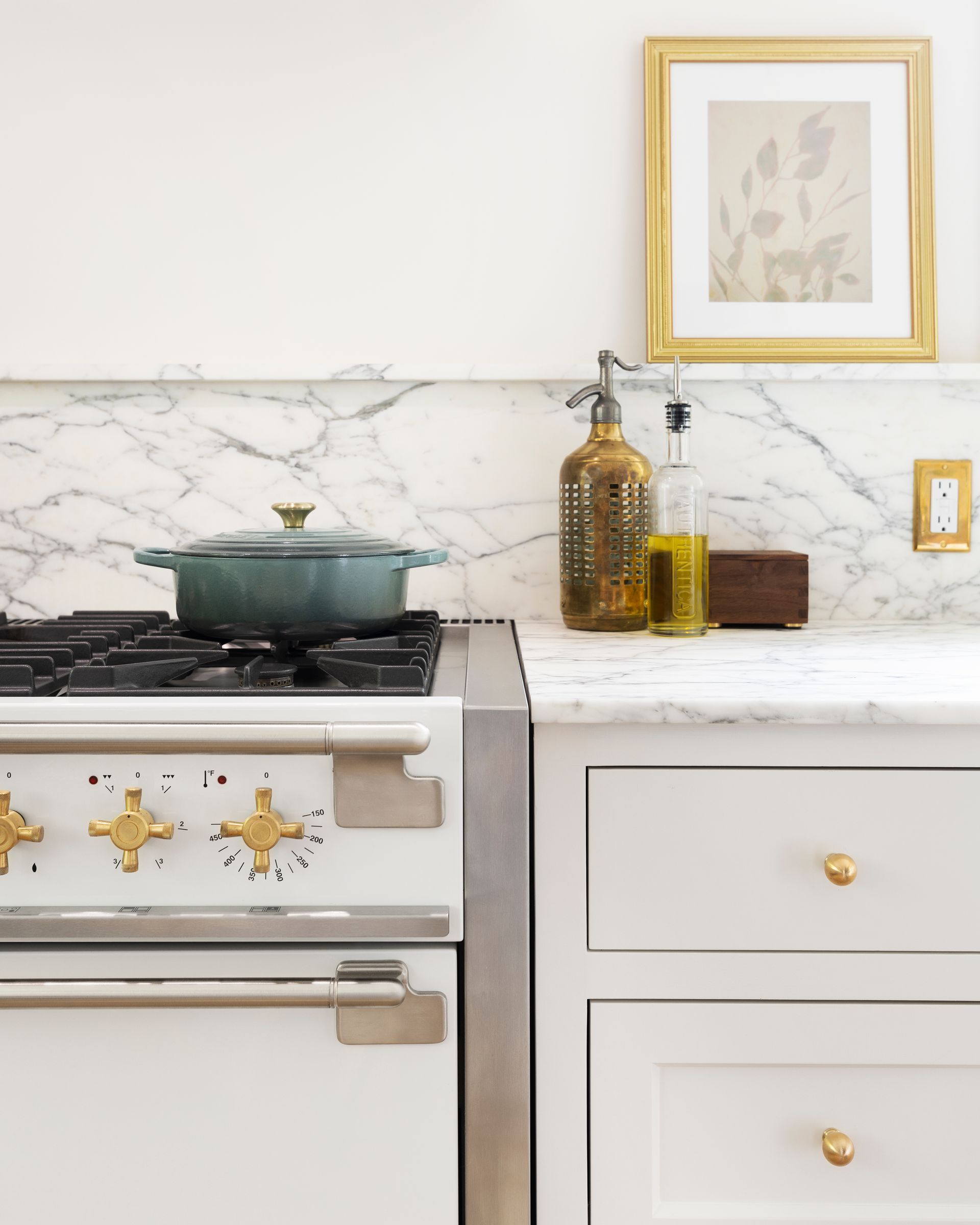 Close up of the range and the base cabinets to the right, with cooking oil, a blue dutch oven and framed artwork on the picture ledge above the backsplash. 