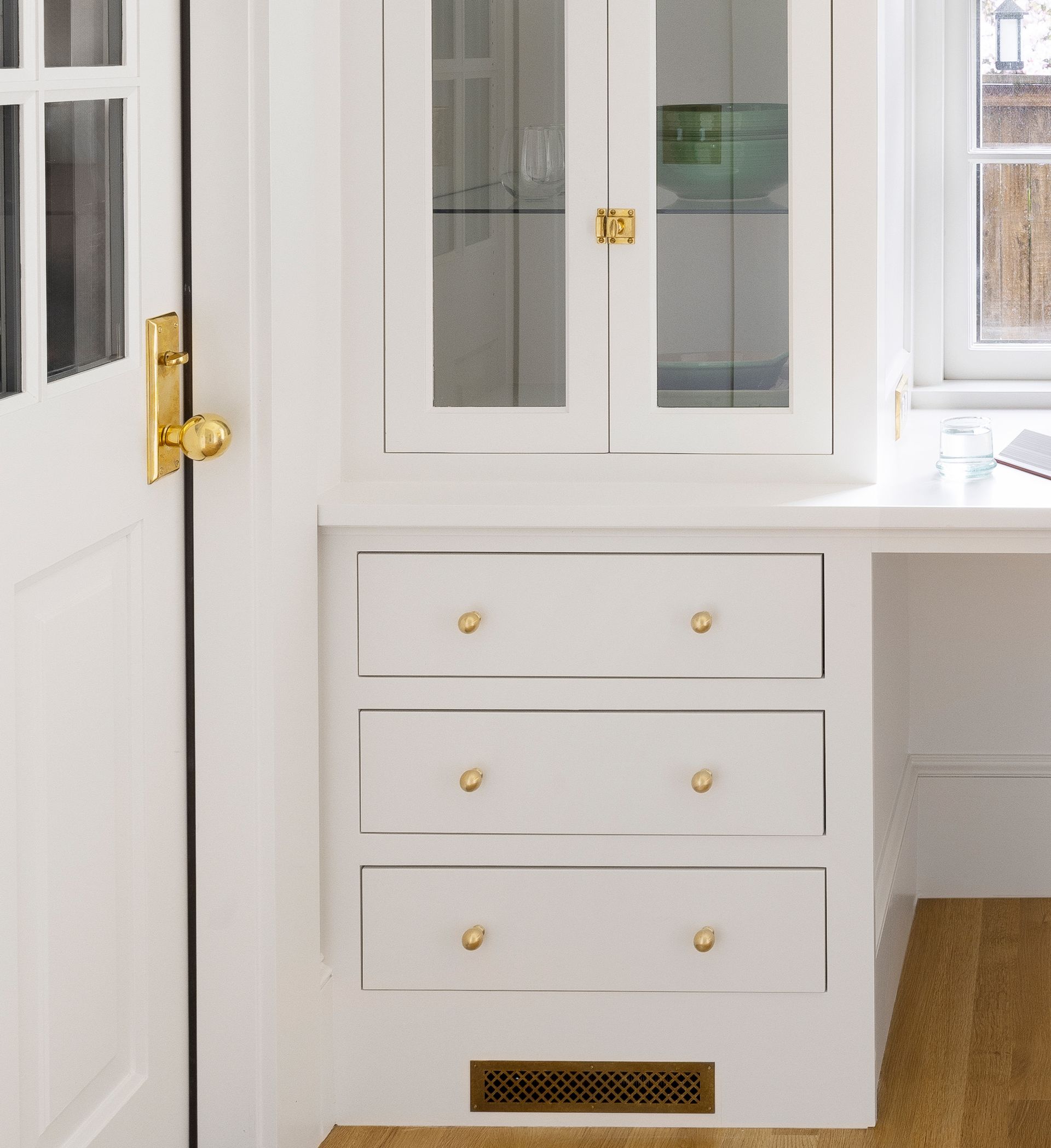 Close up of the office cabinetry, with three drawers below the worktop and glass-paned doors at the uppers. 