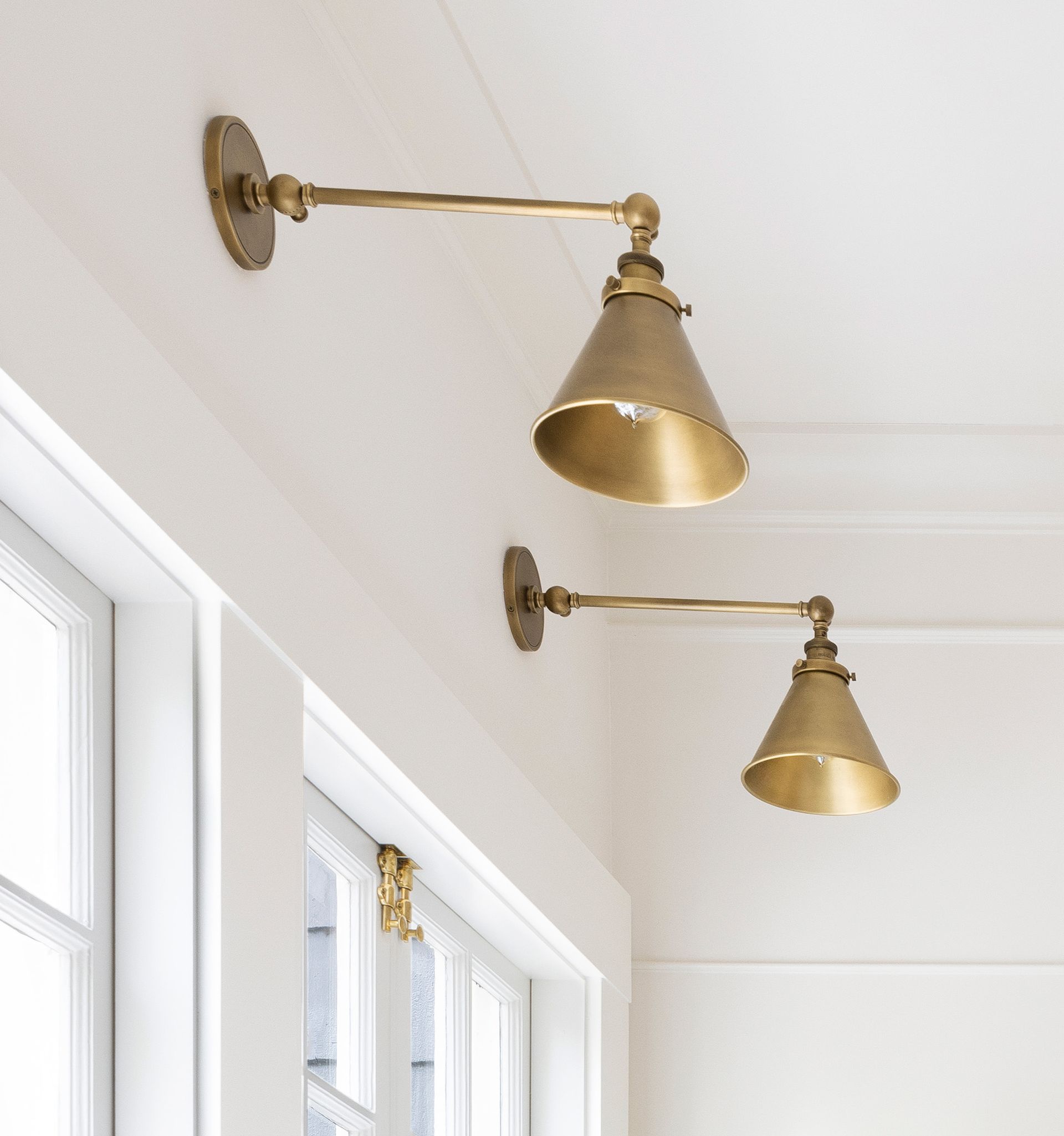 Above two kitchen windows are a pair of unlacquered brass library sconces with cone shaped shades for a warm glow.