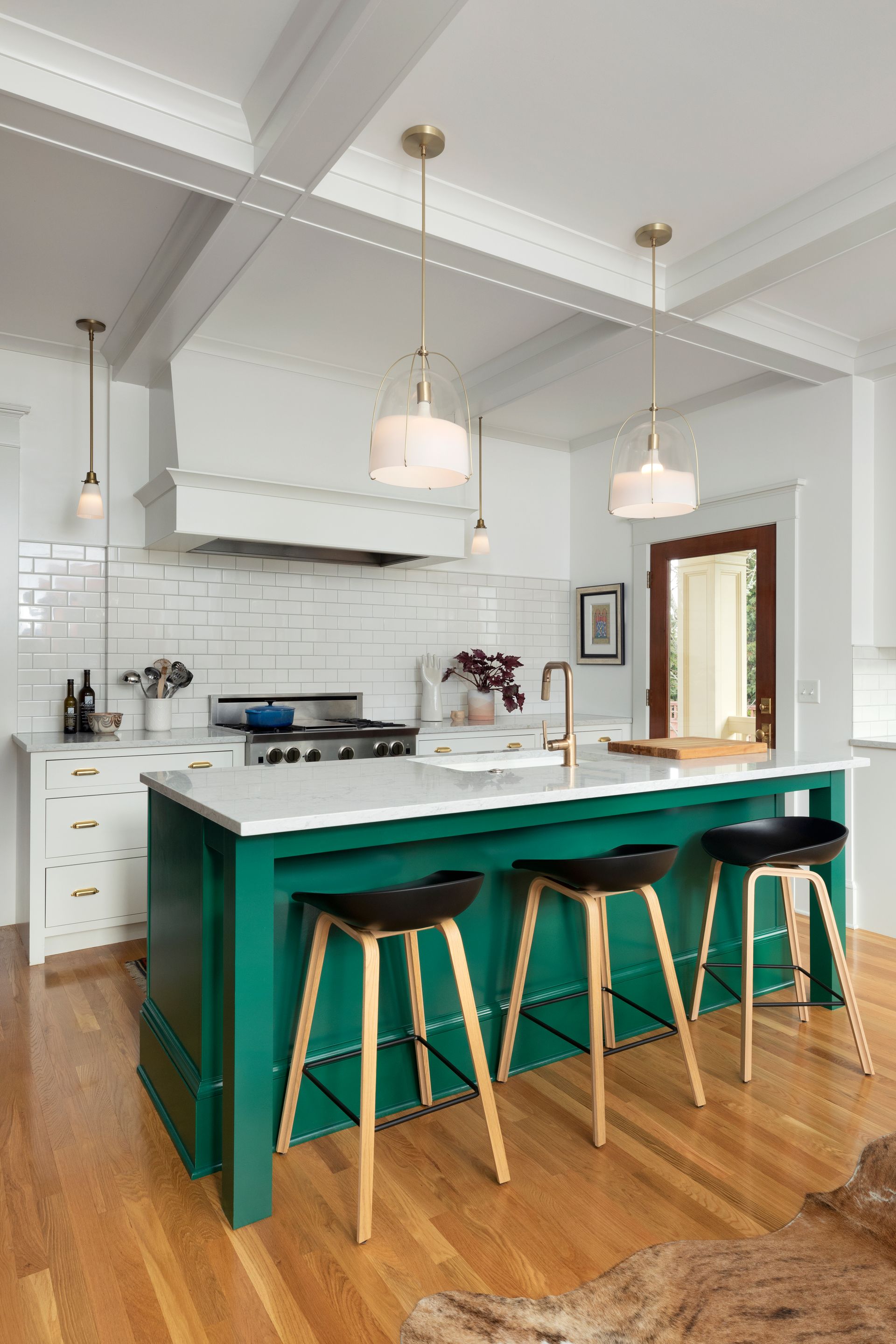 An emerald-green island anchors a white kitchen range wall and provides seating for three.