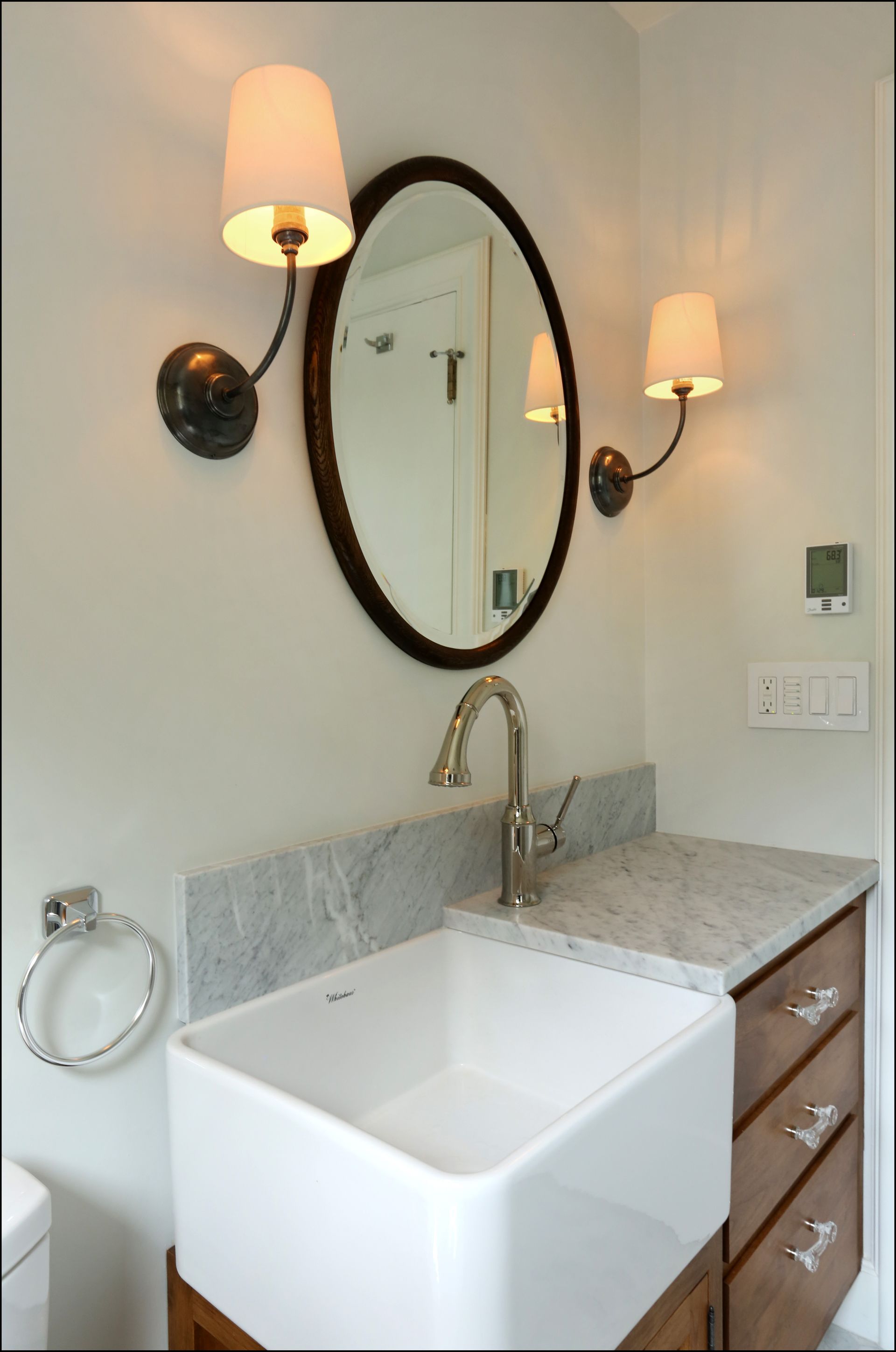 Bathroom vanity with oval mirror, wall sconces, white sink, and marble countertop