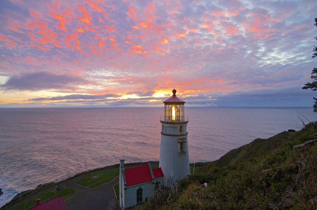 A lighthouse on a hill overlooking the ocean at sunset.