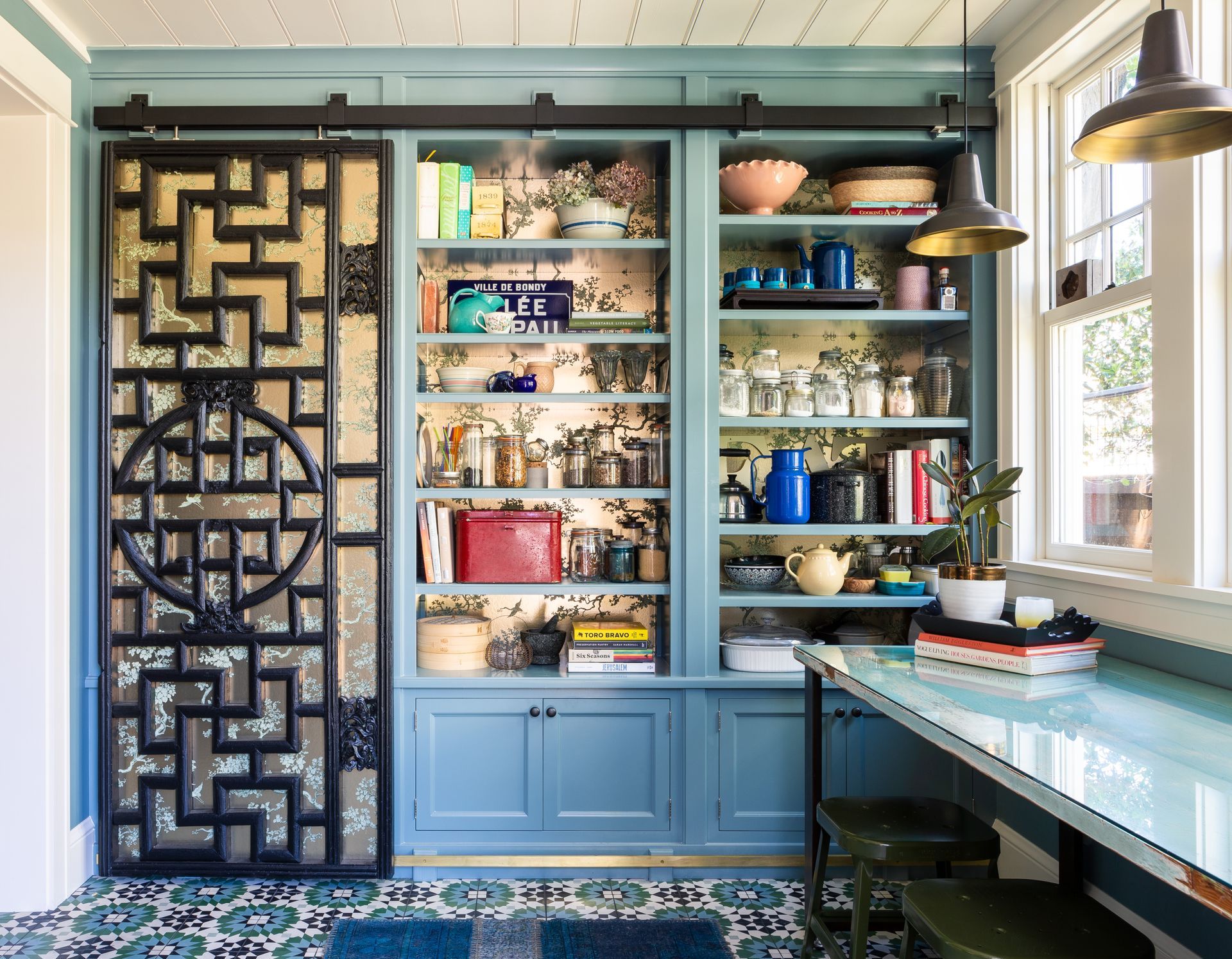In this 1909 Sellwood bungalow, Arciform added a floor-to-ceiling pantry along one wall of an entry space adjacent to the kitchen. A vintage Chinese screen serves as a sliding door, which is wallpapered, like the back of the cabinets, with a shimmering gold wallpaper. 