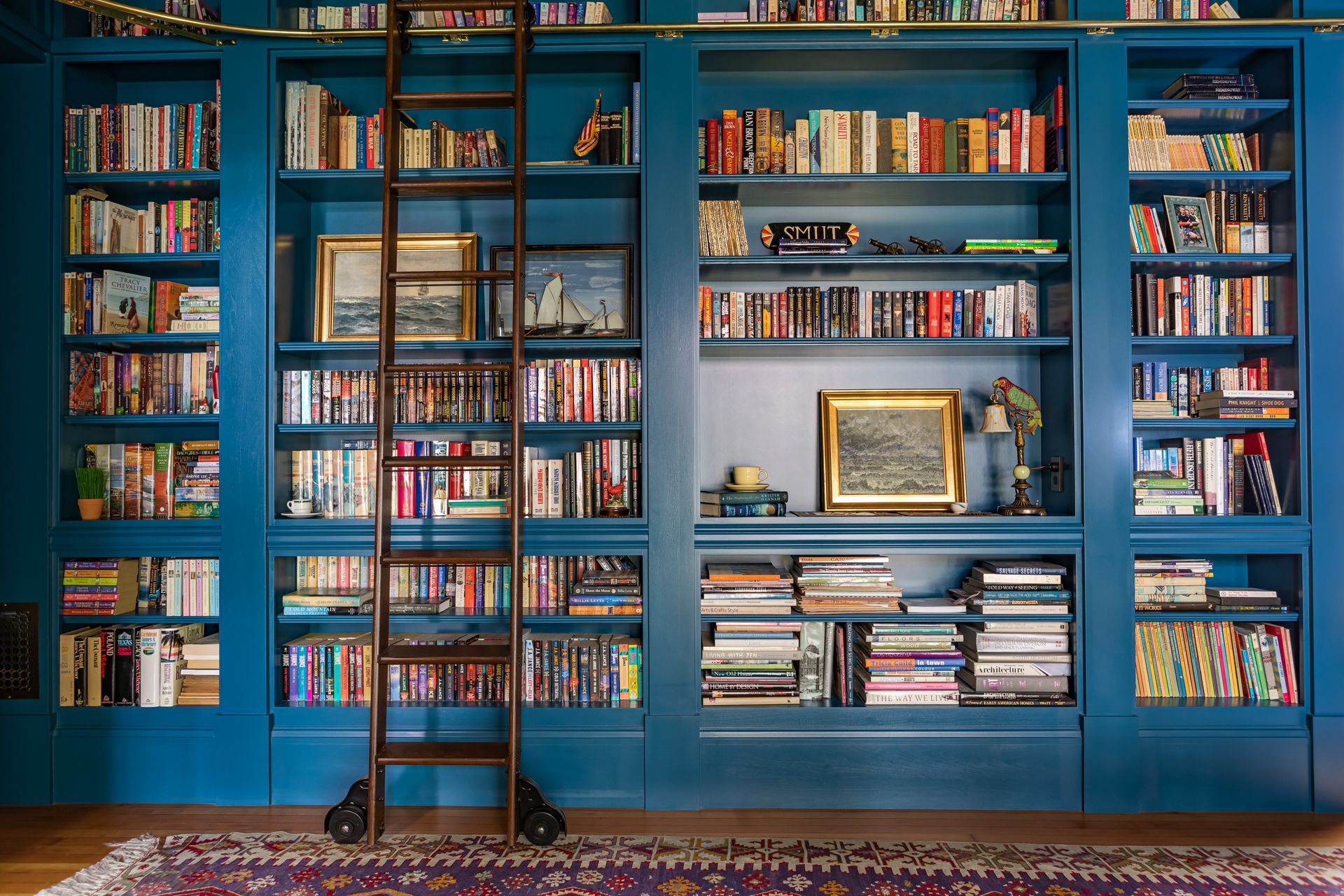 Custom library bookcases by Arciform filled with many books and seascapes, accessed with a rolling library ladder.