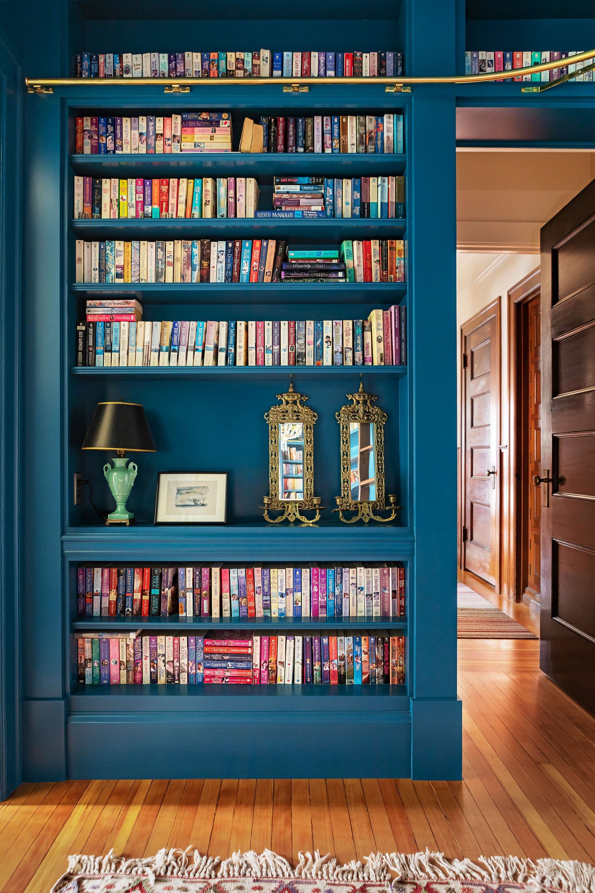 Blue built-in bookshelf filled with books and decor next to a hallway with wooden floors.