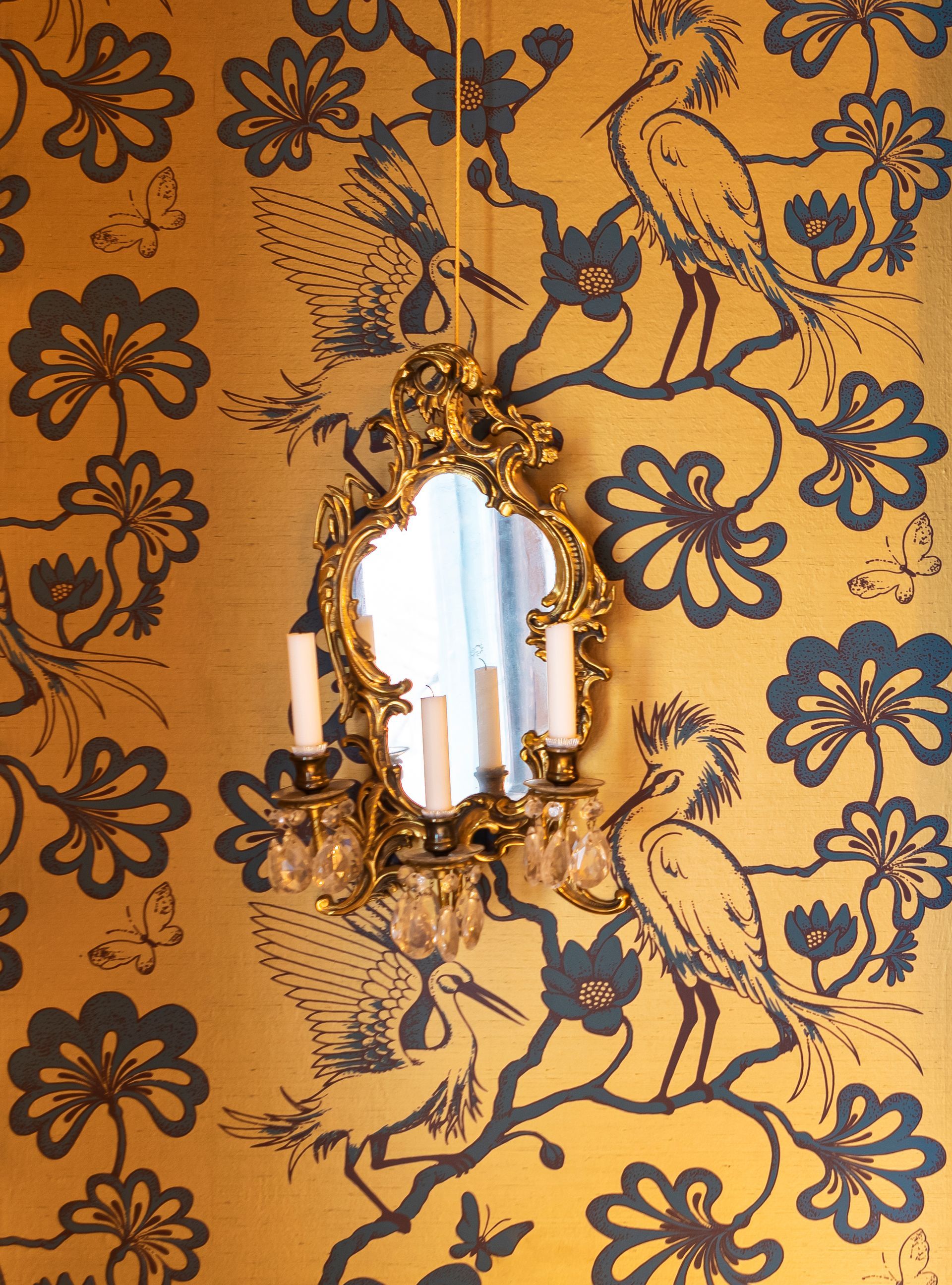 Gold and dark teal Florence Broadhurst wallpaper featuring cranes with vintage candelabra mirror.