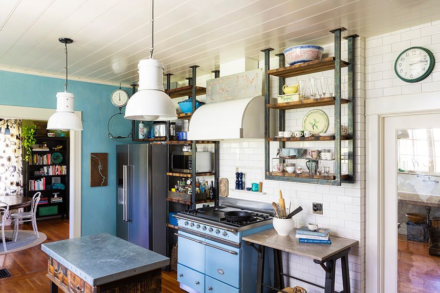 The LaCanche range is flanked by custom, ceiling-mounted steel and wood open shelving and has a glossy, enameled range hood above.