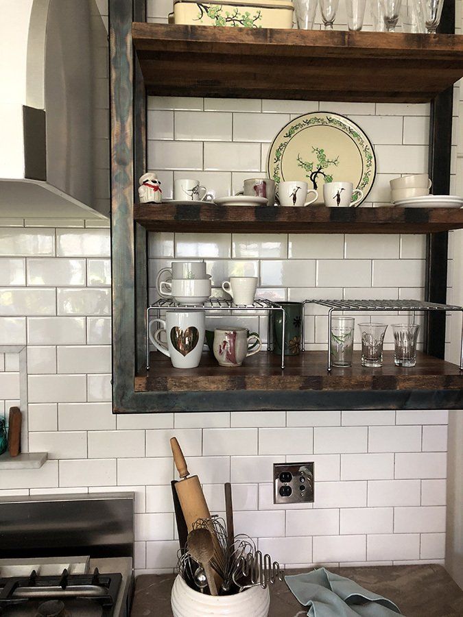 A kitchen with a wooden shelf filled with dishes and utensils.
