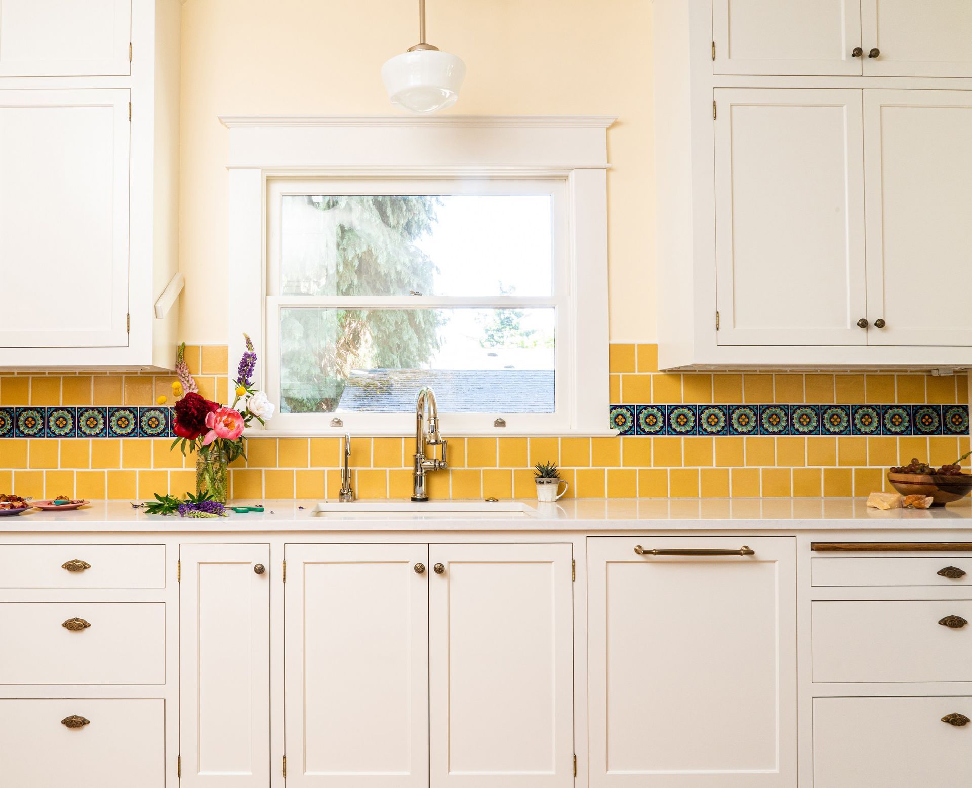 A sunny kitchen with tiled yellow backsplash at the sink, under a window.