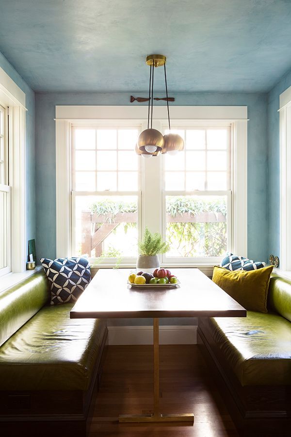 The new kitchen nook has windows with extra deep sills, a custom table with a brass leg, and green leather benches.