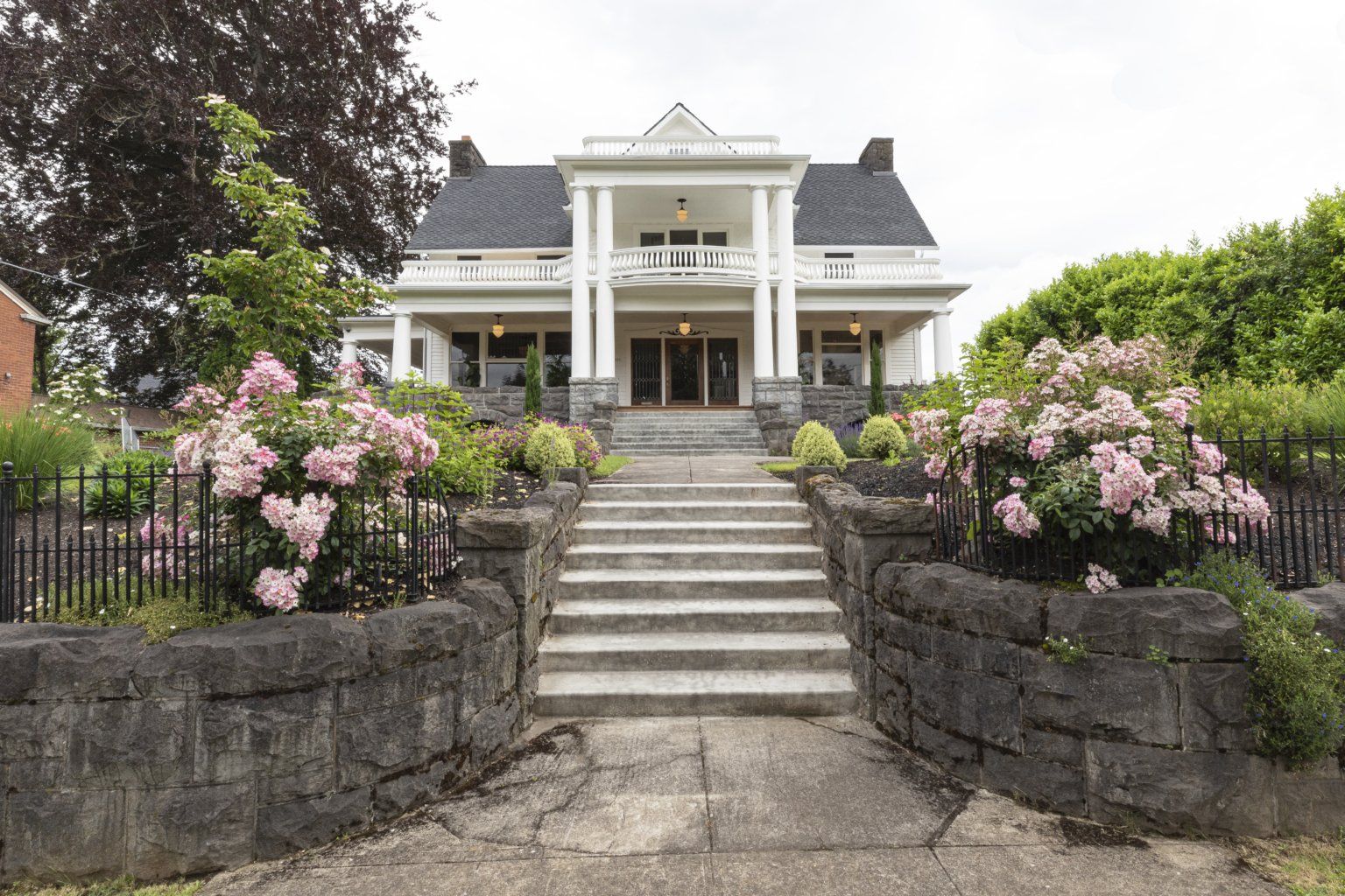 A basalt rock wall borders the Jacob H. & Etna M. Cook house along the sidewalk; the brick foundation is also faced with basalt