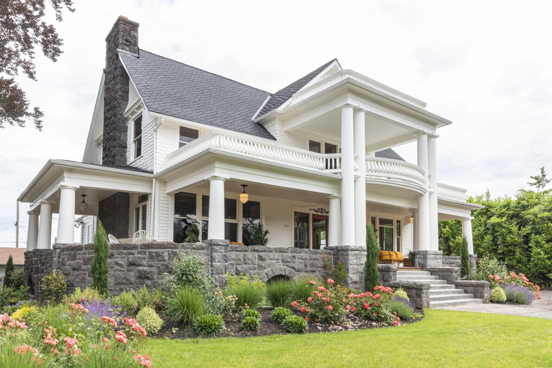 A large white house with columns and a large porch surrounded by flowers.