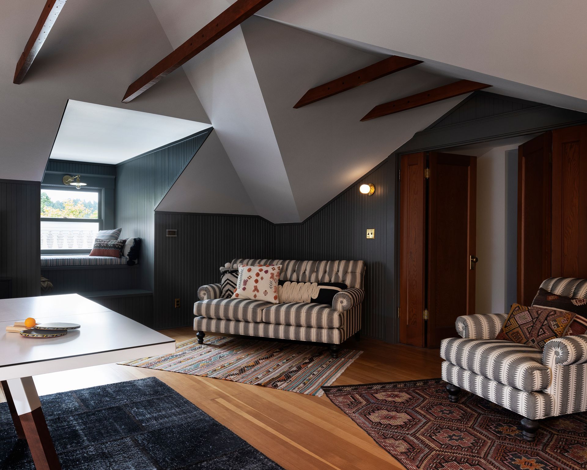 Multiple ceiling angles, open cross braces, and the contrast between dark-painted paneling and white ceilings give this attic playroom a dynamic presence.