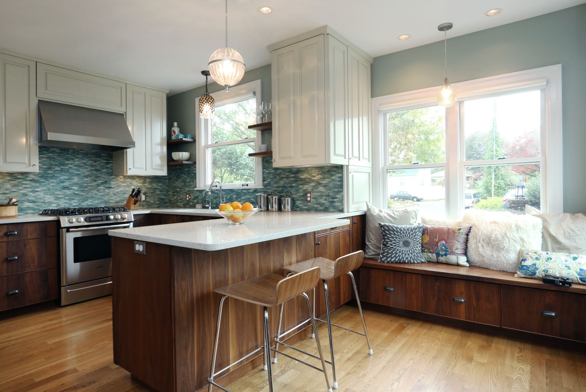 With the window seat on the right, looking past the island into the kitchen with walnut lower cabinets, white uppers and wood floors