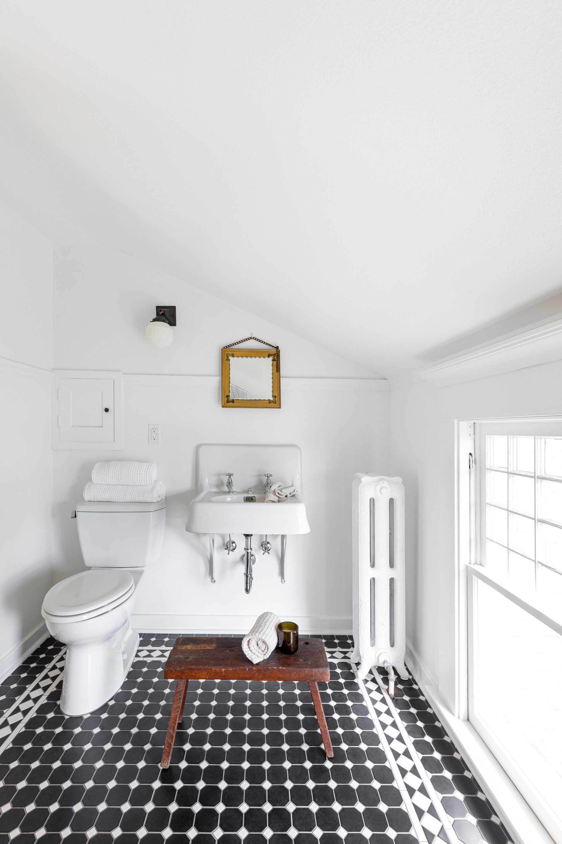 Charming restored bathroom with a black and white patterned tile bath with a border.