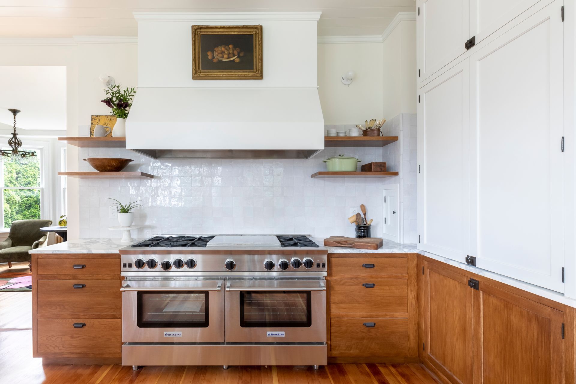 The kitchen's stainless steel range is generous enough to prep for entertaining a crowd. Glossy white zellige tile and a beautiful custom range hood contrast with the wood tones in the room.