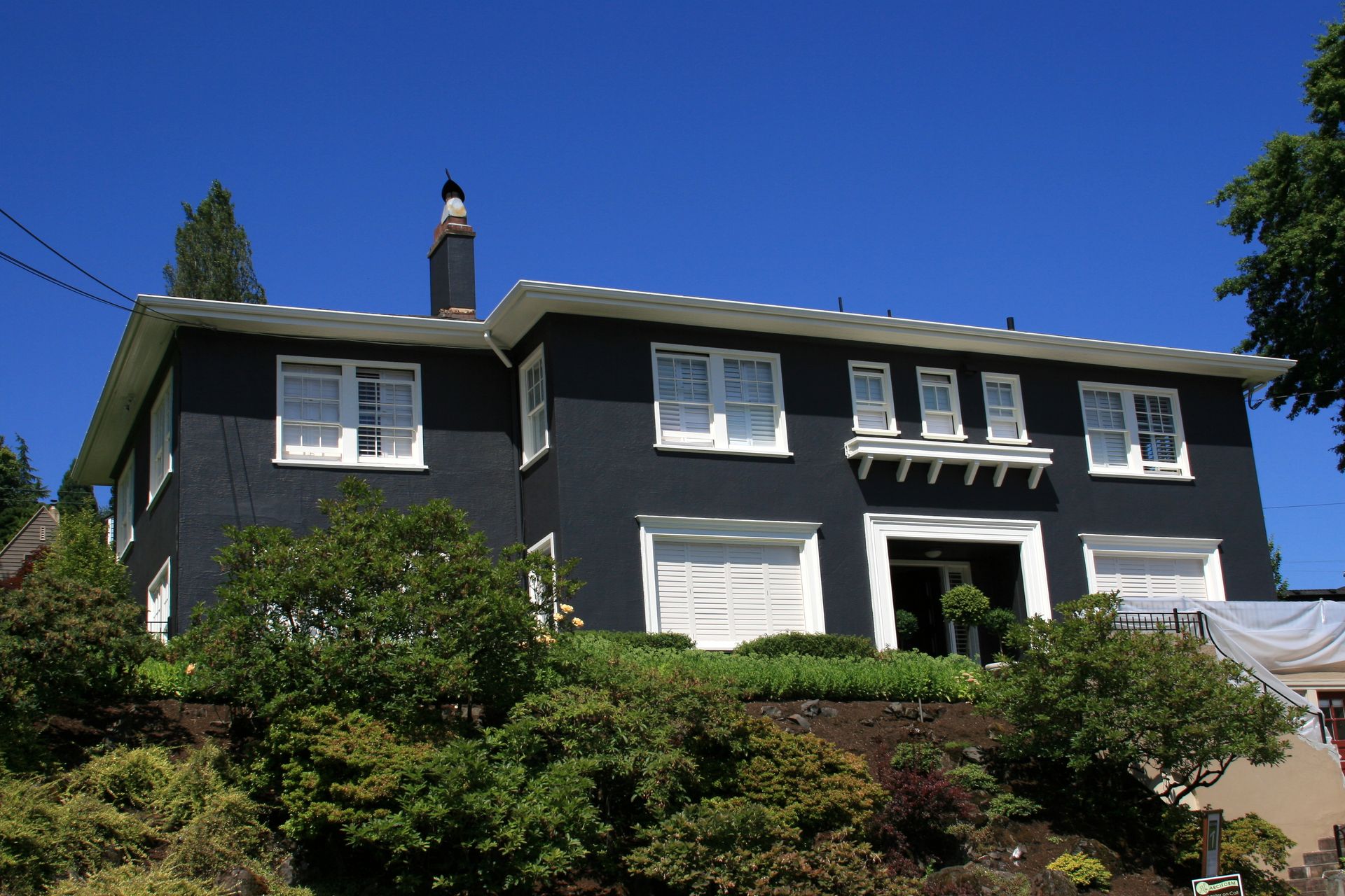 Gray two-story house with white trim and a chimney, seen from a landscaped front yard under a blue sky