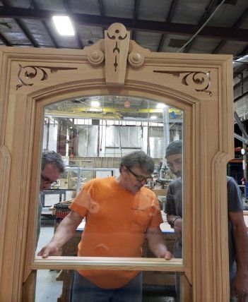 Two men are working on a wooden window frame in a factory.