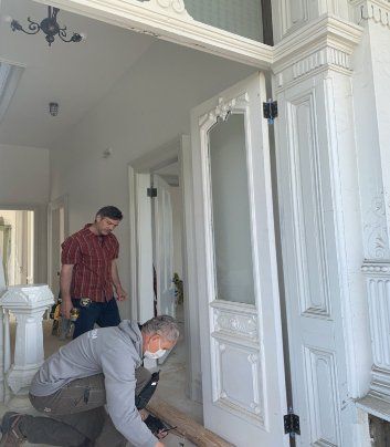 Two men are working on a door in a hallway.