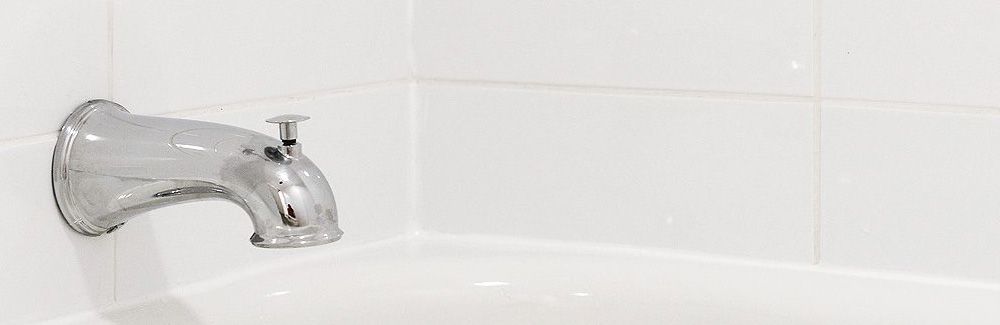 Clean white caulk in bath tub with white tile.
