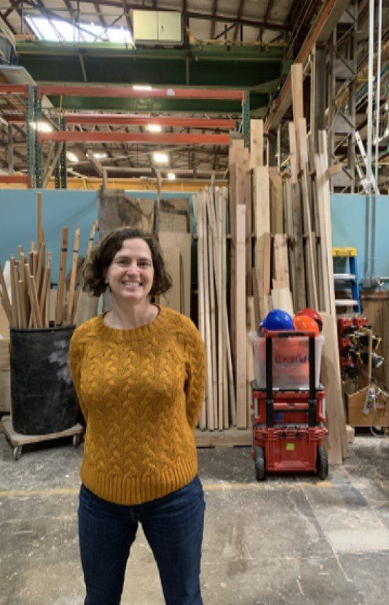 A woman in a yellow sweater is standing in a warehouse.